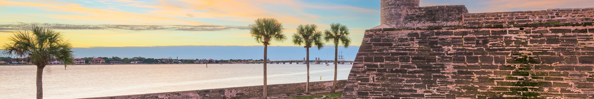 Coastal fort wall with palm trees at sunset